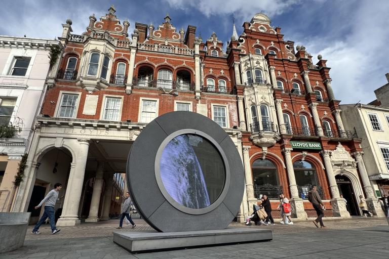 A large circular sculpture in a town centre beside historic building