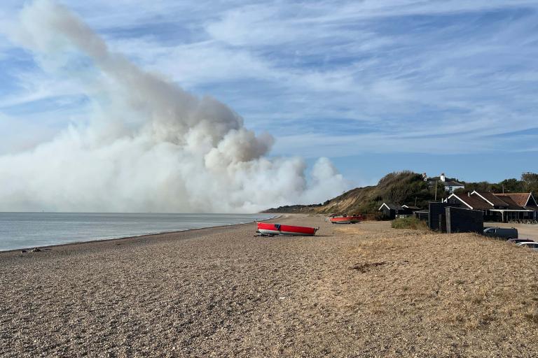 A beach in summer with smoke appearing in the sky in the background