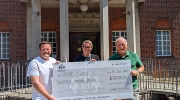 Three people holding a large cheque for £17,000