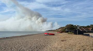 A beach in summer with smoke appearing in the sky in the background